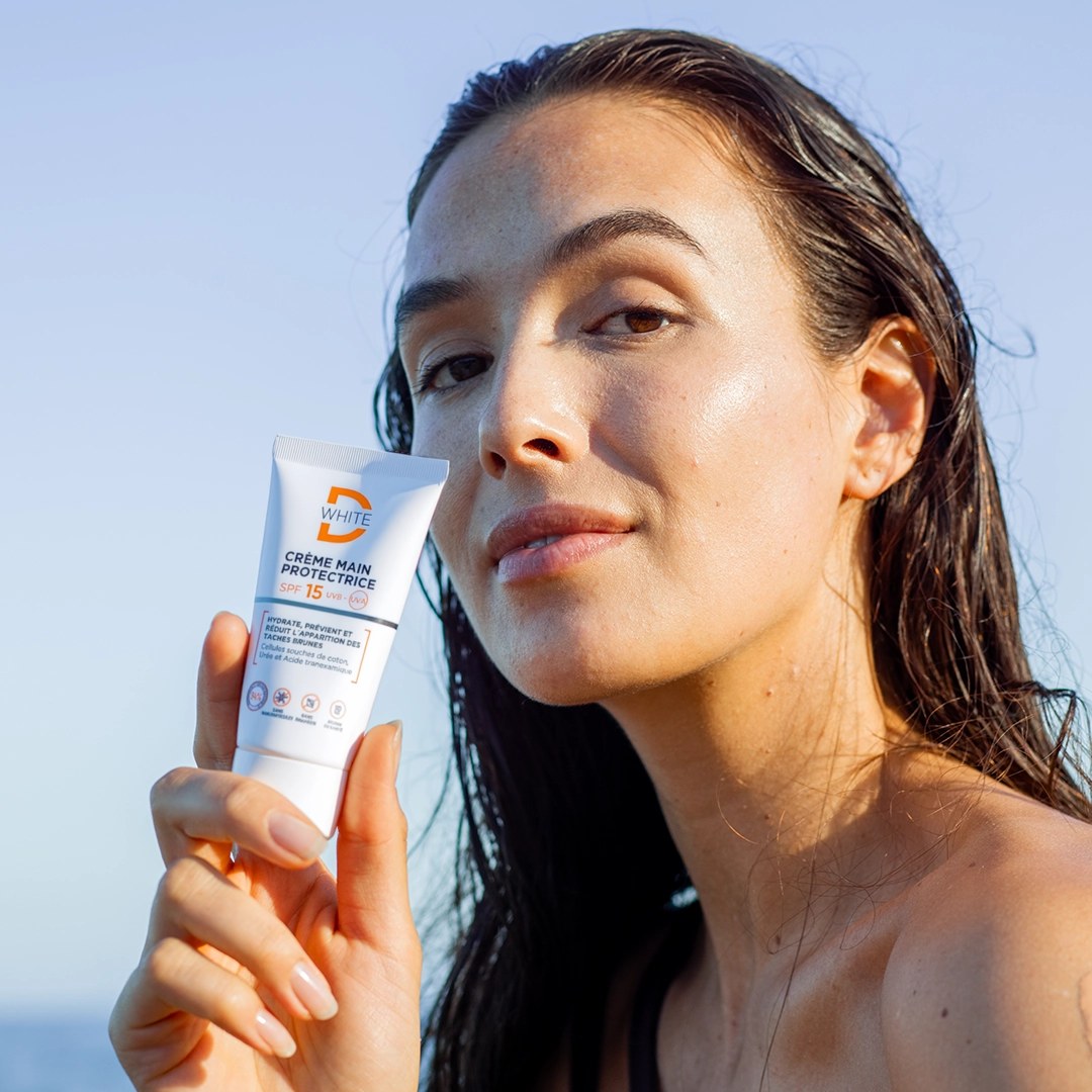 Crème solaire D-White tenue par une femme en bord de mer